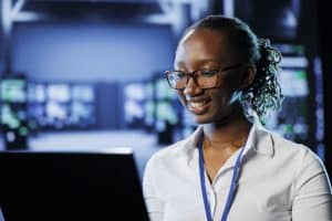 A cybersecurity professional working on a laptop in a server room, ensuring data security and system functionality.